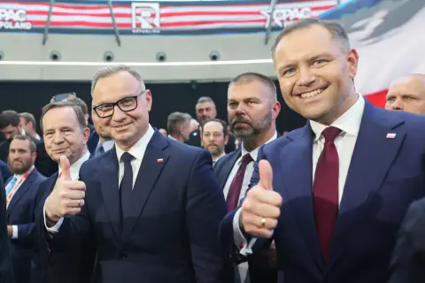 Dwóch mężczyzn w garniturach, jeden z nich pokazuje kciuk w górę. W tle widać napis CPAC Poland. Długość kadencji prezydenta jest tematem dyskusji.