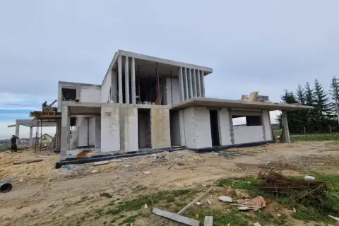 Budowa nowoczesnego domu z betonu i białych pustaków, w tle las.