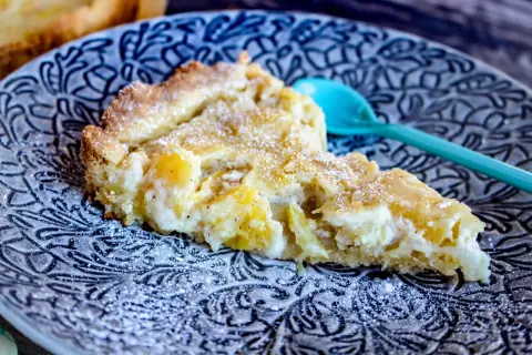 En bit ananaspaj med pudersocker på en mönstrad tallrik. Perfekt för ett ananaspaj recept.