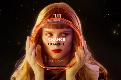 Kobieta z rudymi włosami trzyma okrągłą butelkę perfum Chanel Chance Eau Vive.