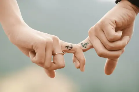 Dłonie z tatuażami kotwic, symbolizujące trwały dotyk w relacjach damsko-męskich. Pierścionek na palcu.
