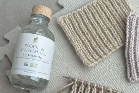 Flasche "Wool & Cashmere" Bio-Waschmittel neben gestrickten Proben. Ideal für die Frage: Pullover waschen welches Programm?