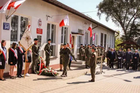 Uroczystość przed budynkiem szkoły z udziałem wojska, uczniów i gości.