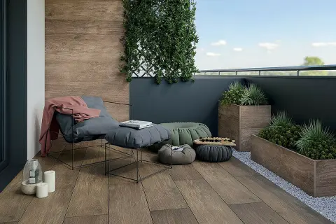 Drewnopodobne płytki na balkon tworzą przytulną atmosferę. Wygodny fotel, pufy i rośliny zapraszają do relaksu.