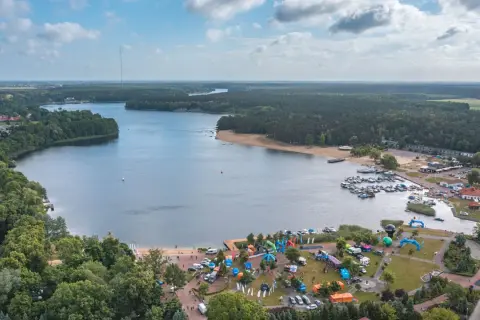 Widok na jezioro Otmuchowskie z lotu ptaka. Widać plażę, przystań jachtową, las i miasteczko z atrakcjami.