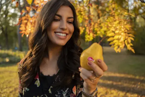 Donna sorridente tiene una pera gialla, uno dei cibi che fanno fare la cacca subito, in un parco autunnale.
