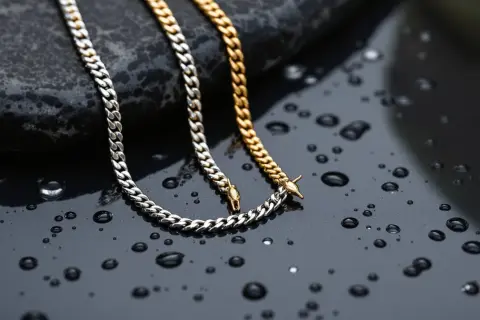 Dos cadenas, una plateada y otra dorada, descansan sobre una superficie oscura con gotas de agua, demostrando que el acero inoxidable se puede mojar sin problemas.