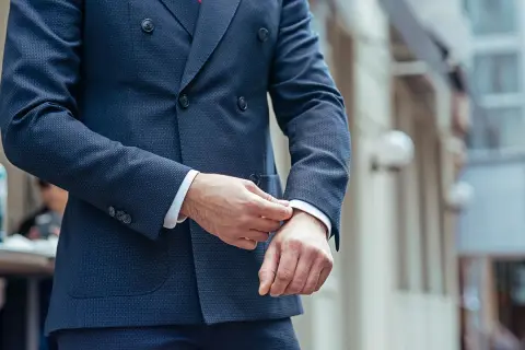 Uomo che sistema il polsino della sua giacca blu, un perfetto abbinamento giacca blu uomo per un look elegante.