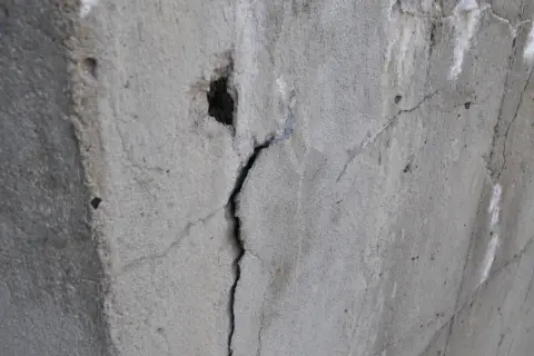 Pęknięty beton z widocznym otworem i drobnymi ubytkami.
