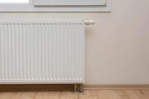 Biały grzejnik pod oknem, termostat ustawiony na 60 stopni, ale grzejniki letnie.