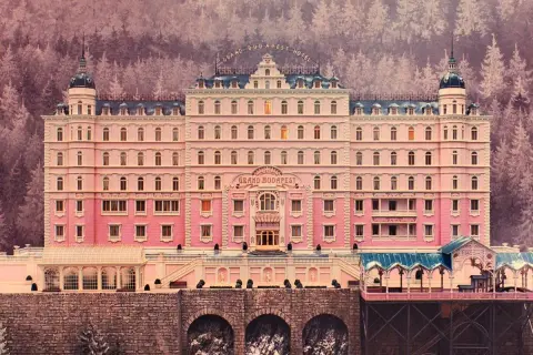 A grand pink hotel with a distinct Wes Anderson aesthetic, nestled in a snowy, purple-hued forest.
