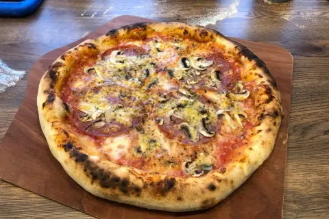 Chrupiąca pizza z pieczarkami i salami na drewnianej desce.
