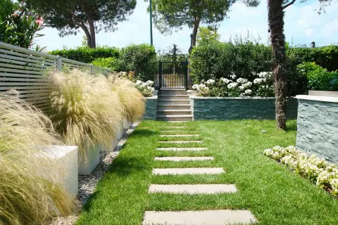 Un bellissimo giardino progetto con un sentiero di lastre di pietra, erba verde, cespugli fioriti e un muretto in pietra.