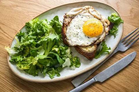 Ein herzhafter Croque Madame mit Spiegelei, Käse und Toast, serviert mit frischem Salat.