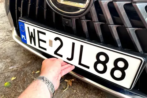 Dłoń poprawia tablicę rejestracyjną z numerem WE 2JL88, przygotowując wniosek o rejestrację pojazdu.