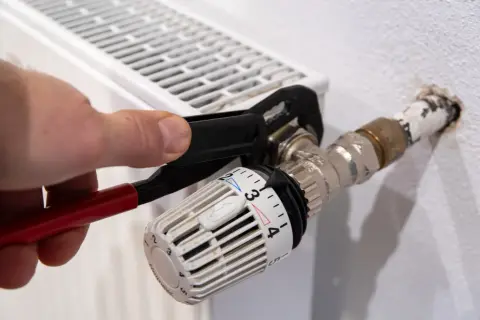 Hand uses pliers to heizungsventil tauschen. Der Thermostatkopf ist auf Stufe 3 eingestellt.