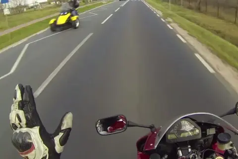 Pozdrowienie motocyklistów na drodze. Żółty pojazd trójkołowy mija motocyklistę.