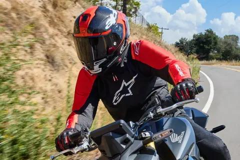 Motocyklista w czerwono-czarnym kasku i kurtce jedzie po krętej drodze.