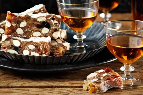 Panforte-bitar med mandlar och torkad frukt, pudrade med florsocker, serveras med ett glas gyllene likör. Ett härligt panforte recept att njuta av.