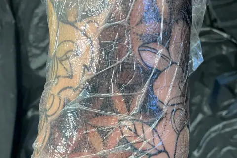 Frische Tattoo-Haut geht ab, bedeckt mit Folie. Das Motiv zeigt dunkle Schattierungen und klare Linien.