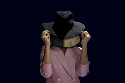 Sia w różowym żakiecie i kapeluszu zasłaniającym twarz, z blond włosami i frędzlami. Tekst "cheap thrills" idealnie pasuje do tej stylizacji.