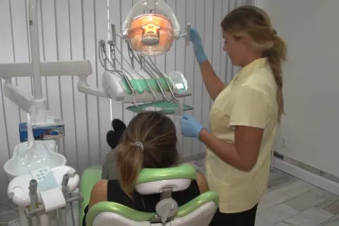 Dentystka przygotowuje znieczulenie w sprayu dla pacjentki siedzącej na fotelu.