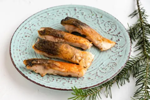 Vier goldbraun gebratene Karpfenfilets mit Haut liegen auf einem mintgrünen Teller.