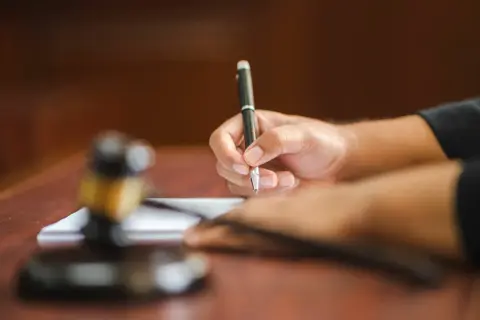 Dłoń pisze piórem na papierze, obok młotek sędziowski. Tak pracuje referendarz sądowy, kto to?