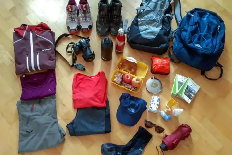 Packliste Wanderurlaub: Wanderschuhe, Rucksäcke, Kleidung, Kamera, Verpflegung und Karten für ein Abenteuer in den Bergen.