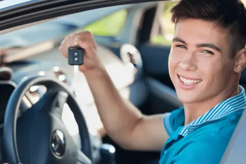 Uśmiechnięty młody mężczyzna trzyma kluczyki do swojego pierwszego auta. Idealne jakie auto na pierwsze!