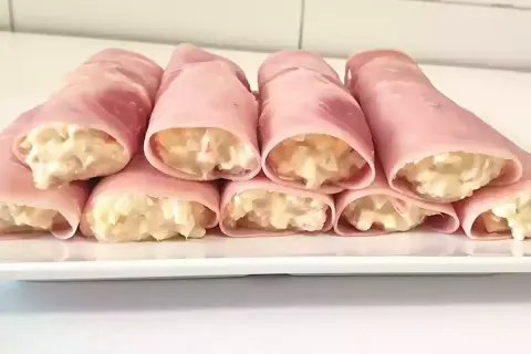 Rollitos de jamón york rellenos de ensaladilla cremosa, presentados en una bandeja blanca.