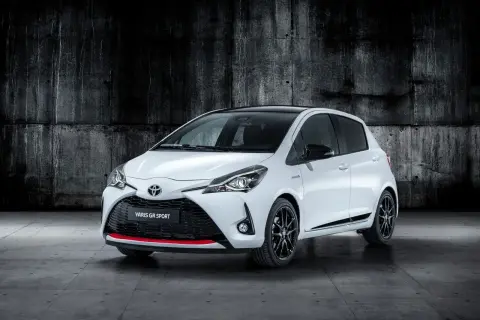 Biały Toyota Yaris GR Sport z czarnym dachem i czerwonymi akcentami, zaparkowany na tle betonowej ściany.