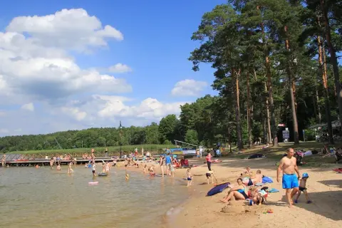 Słoneczny dzień nad jeziorem w Augustowie. Ludzie kąpią się, opalają na plaży i spacerują po molo.