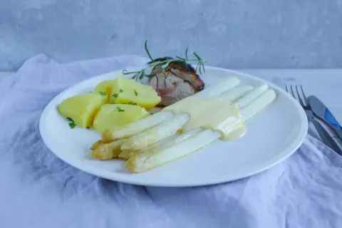 Weißer Spargel mit Sauce Hollandaise, Kartoffeln und Fleisch auf einem Teller.