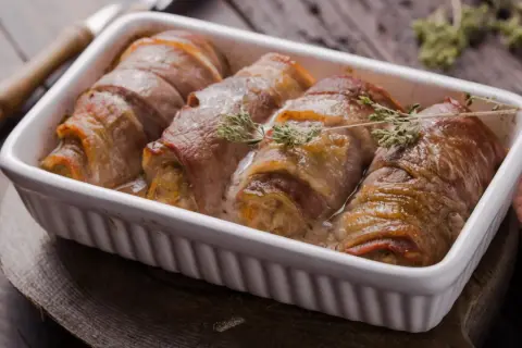 Roladki schabowe pieczone w naczyniu, zawinięte w boczek, z gałązkami tymianku.