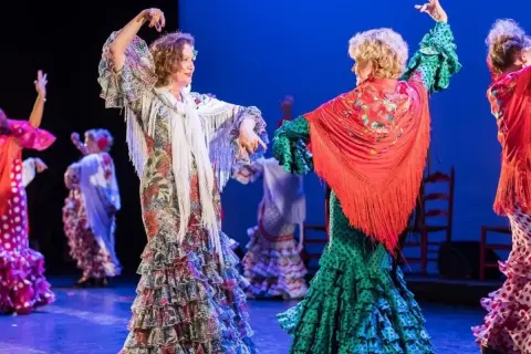 Dos mujeres bailan sevillanas, con volantes y mantones, evocando el origen de esta danza.
