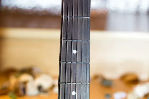 Zbliżenie na gryf gitary z widocznymi progami i strunami. Palce gitarzysty zaraz zaczną tworzyć melodię.