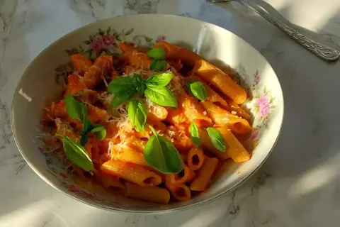 Penne all'arrabiata co to? Pikantny sos pomidorowy z czosnkiem i chili, podany z makaronem penne, posypany parmezanem i świeżą bazylią.