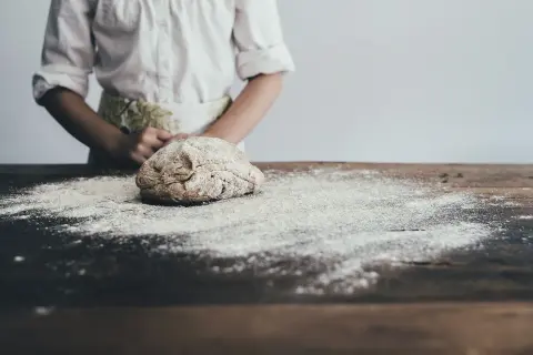 Dziecko w fartuszku przygotowuje ciasto na stole. Zastanawiasz się, jaka mąka jest najzdrowsza? Ta na zdjęciu wygląda na pełnoziarnistą.