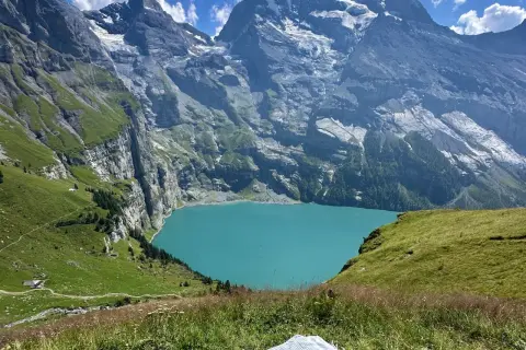 Türkisblaue Oeschinensee Schweiz, umrahmt von steilen, grünen Berghängen und schneebedeckten Gipfeln. Ein idyllischer Ort für Wanderer.