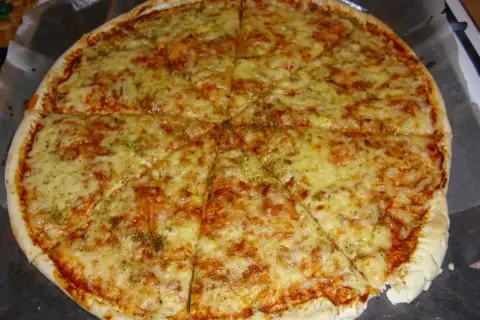 Pyszna, gorąca margarita pizza z ciągnącym się serem i aromatycznymi ziołami, pokrojona na 8 kawałków.