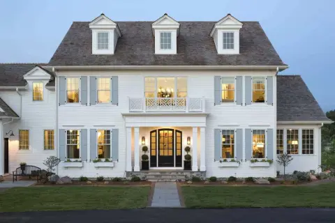 A stately white house with classic colonial architecture, featuring dormer windows, light blue shutters, and a welcoming porch.