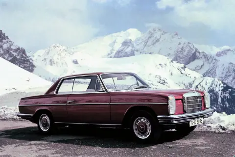 Ciemnoczerwony Mercedes W114 coupe na tle ośnieżonych gór. Klasyka motoryzacji w zimowej scenerii.