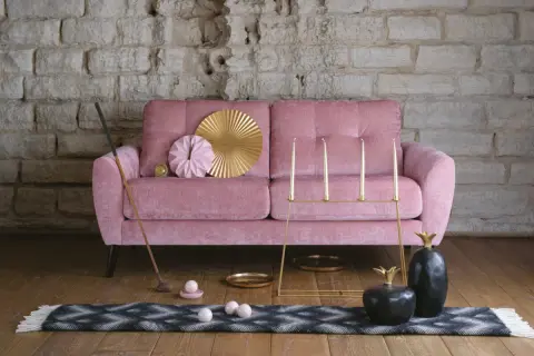 En rosa, **ergonomisk soffa** med dekorativa föremål som en golfklubba, ljusstakar och ananasskulpturer.