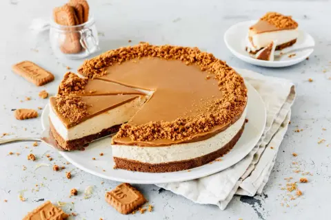 Ein köstlicher Lotus Cheesecake mit Karamellglasur und Keksbröseln. Ein Stück wurde bereits entnommen.