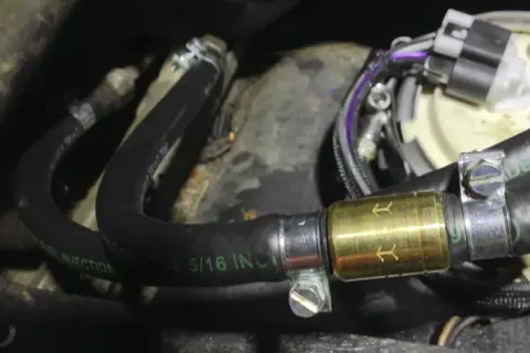 Złoty zawór zwrotny paliwa zamontowany na czarnym wężu paliwowym z oznaczeniem "FUEL INJECTION".