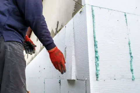 Operaio con guanti rossi applica pannelli per cappotto termico su intonaco esistente.
