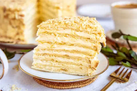 Ein Stück Napoleon Torte mit vielen Schichten Blätterteig und cremiger Füllung, bestreut mit Krümeln.