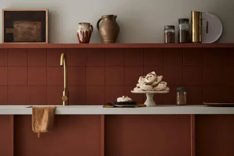 Encimera de cocina pintada en tono terracota, con grifería dorada y detalles decorativos.