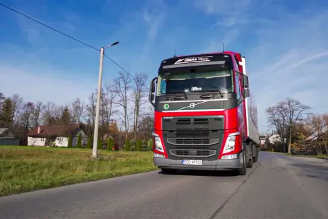 Czerwona ciężarówka Volvo z naczepą jedzie drogą. To praca spedytora, kod zawodu 334101.